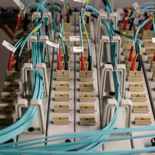 Optical distribution frame with rows of labelled adapter ports connected by aqua fiber patch cords.